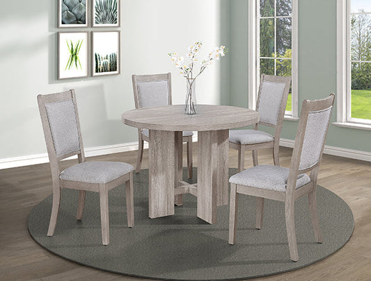 Round light wood dining table with four matching upholstered chairs placed on a circular rug in a bright, modern dining room with large windows and framed botanical art.